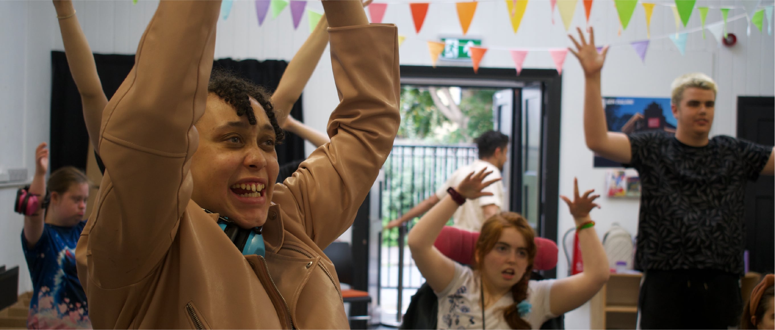 A group of young people raising their hands in a decorated room with colorful bunting.