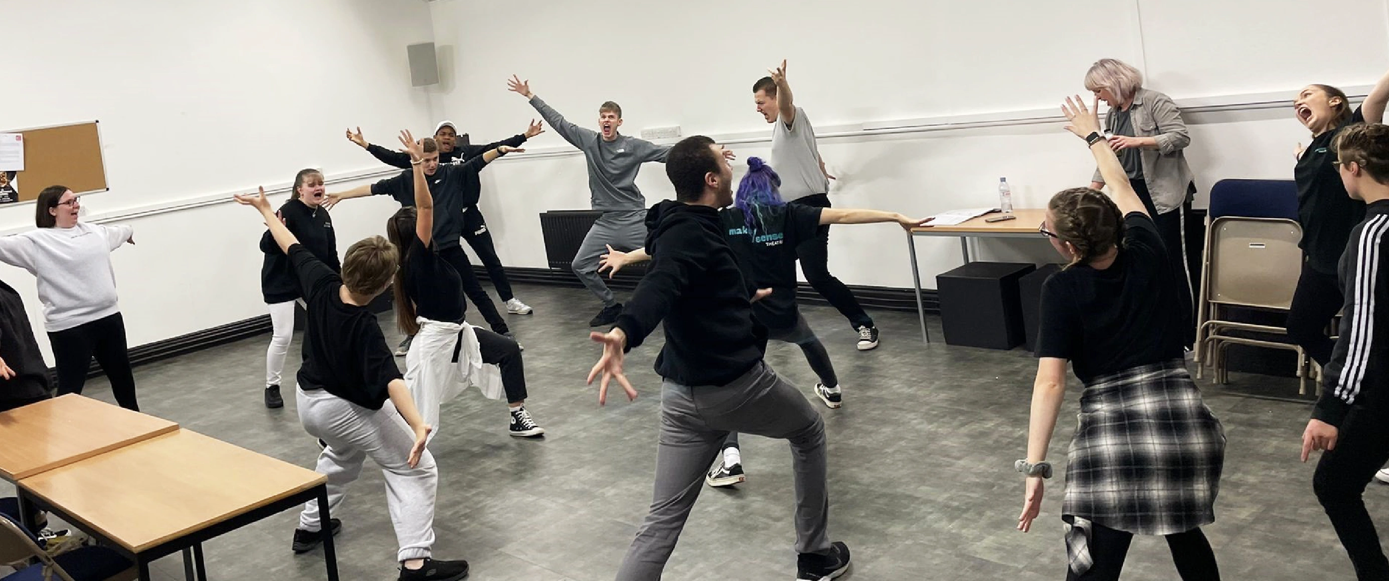 Group of young people in casual clothes energetically practicing theatre movements in a spacious room.
