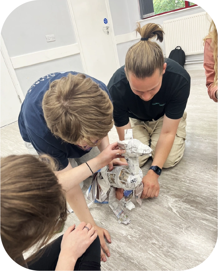 Three people kneeling on the floor manipulating a puppet made from newspaper
