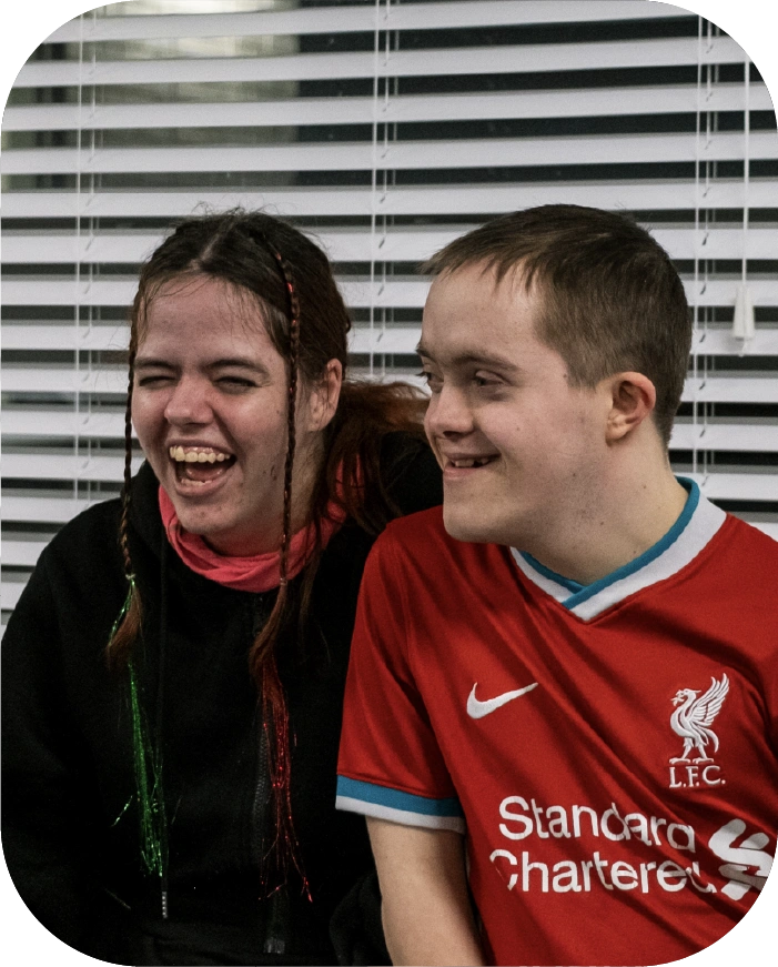 Smiling young woman with braided hair and young man in a red Liverpool FC jersey laughing together.