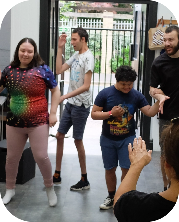 Three young people dancing indoors with one adult guiding and clapping hands.