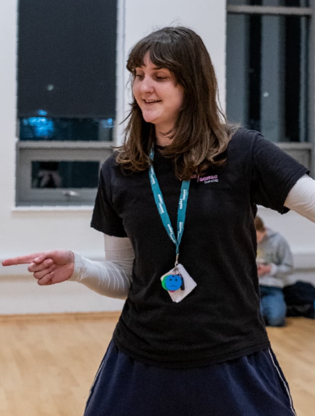 A smiling woman with shoulder-length brown hair wearing a black t-shirt and a lanyard