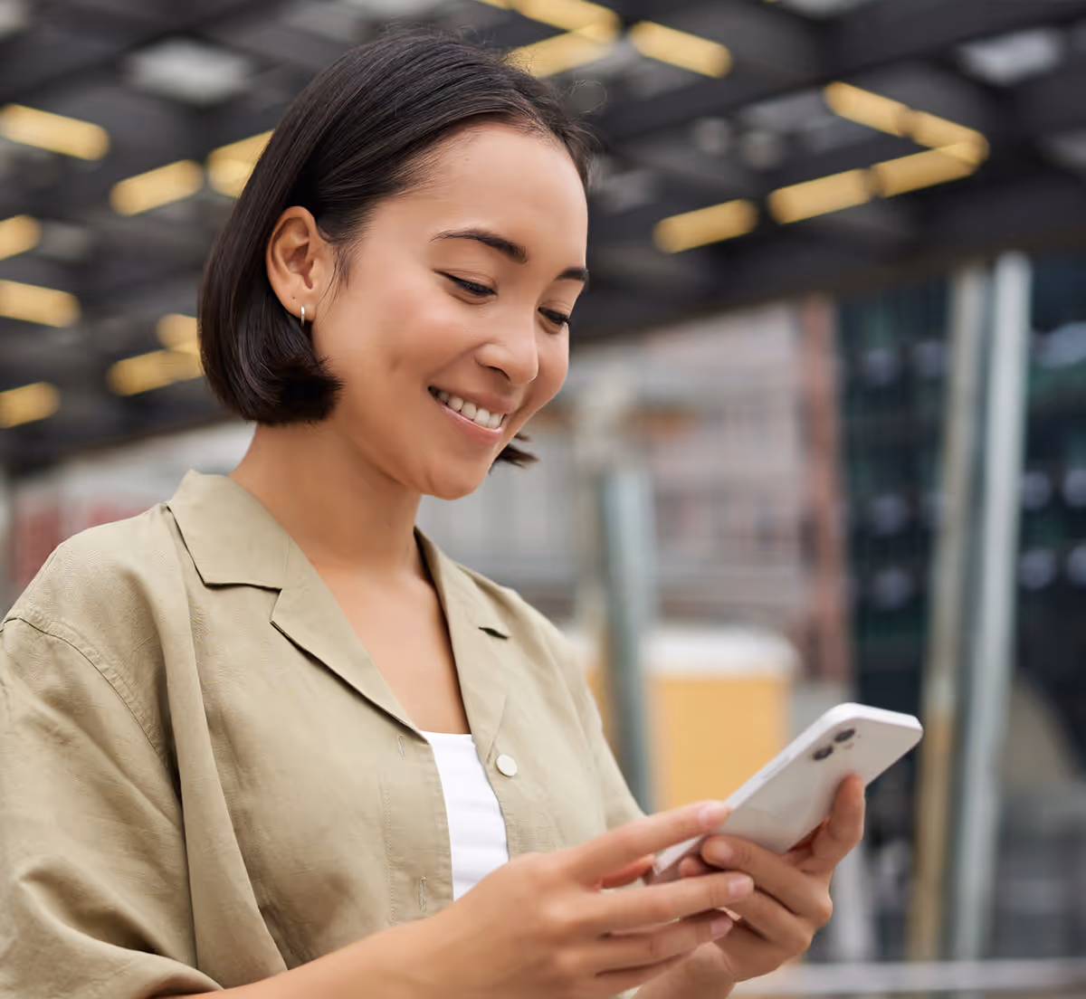 Jeune femme souriante utilisant un smartphone dans un espace urbain couvert.
