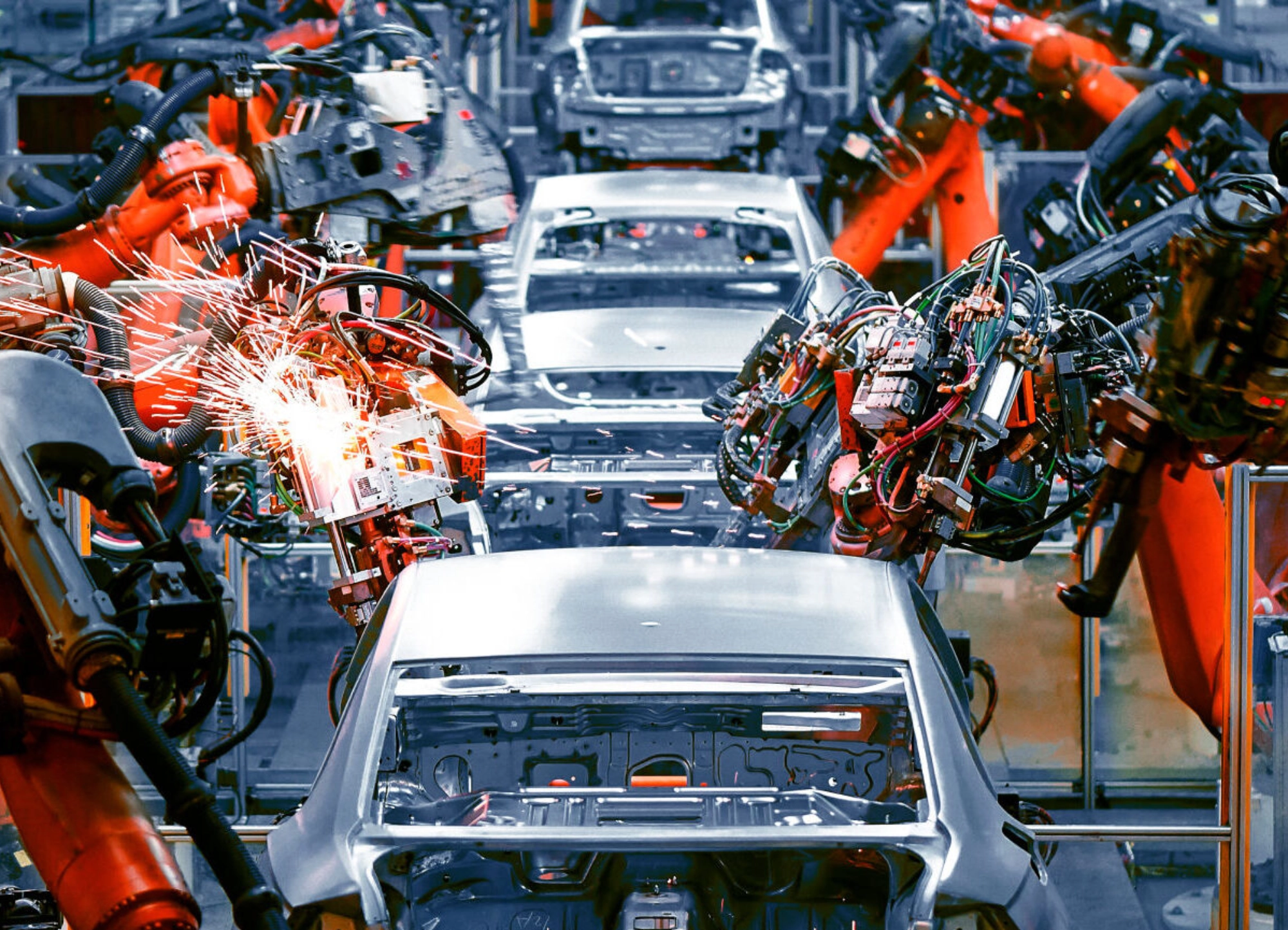 Robotic arms welding car bodies on an automotive production line with sparks flying.