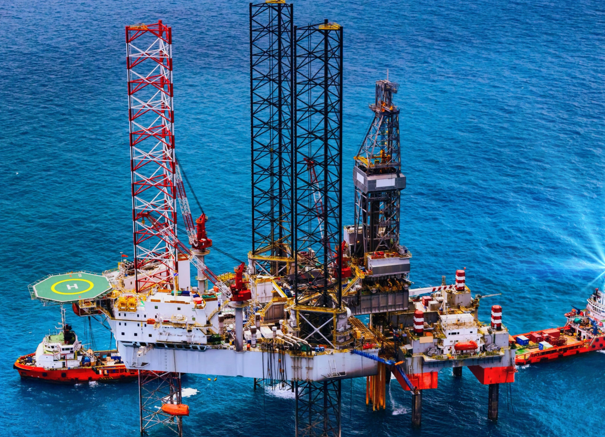 Offshore oil rig platform with a helicopter landing pad and support vessels in blue ocean waters.