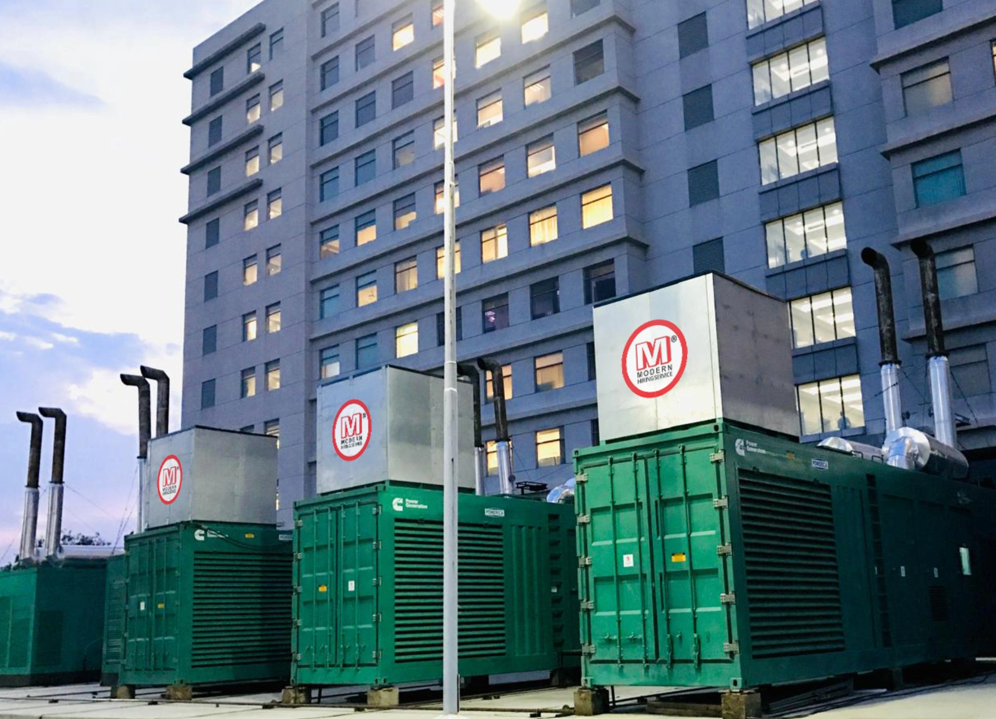 Large green industrial generator with Modern logo and website on side, positioned outdoors near a white wall.
