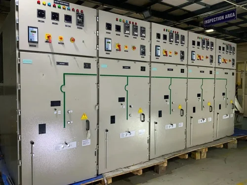 Large teal industrial generator with a yellow and black safety railing in front, placed against a white wall.