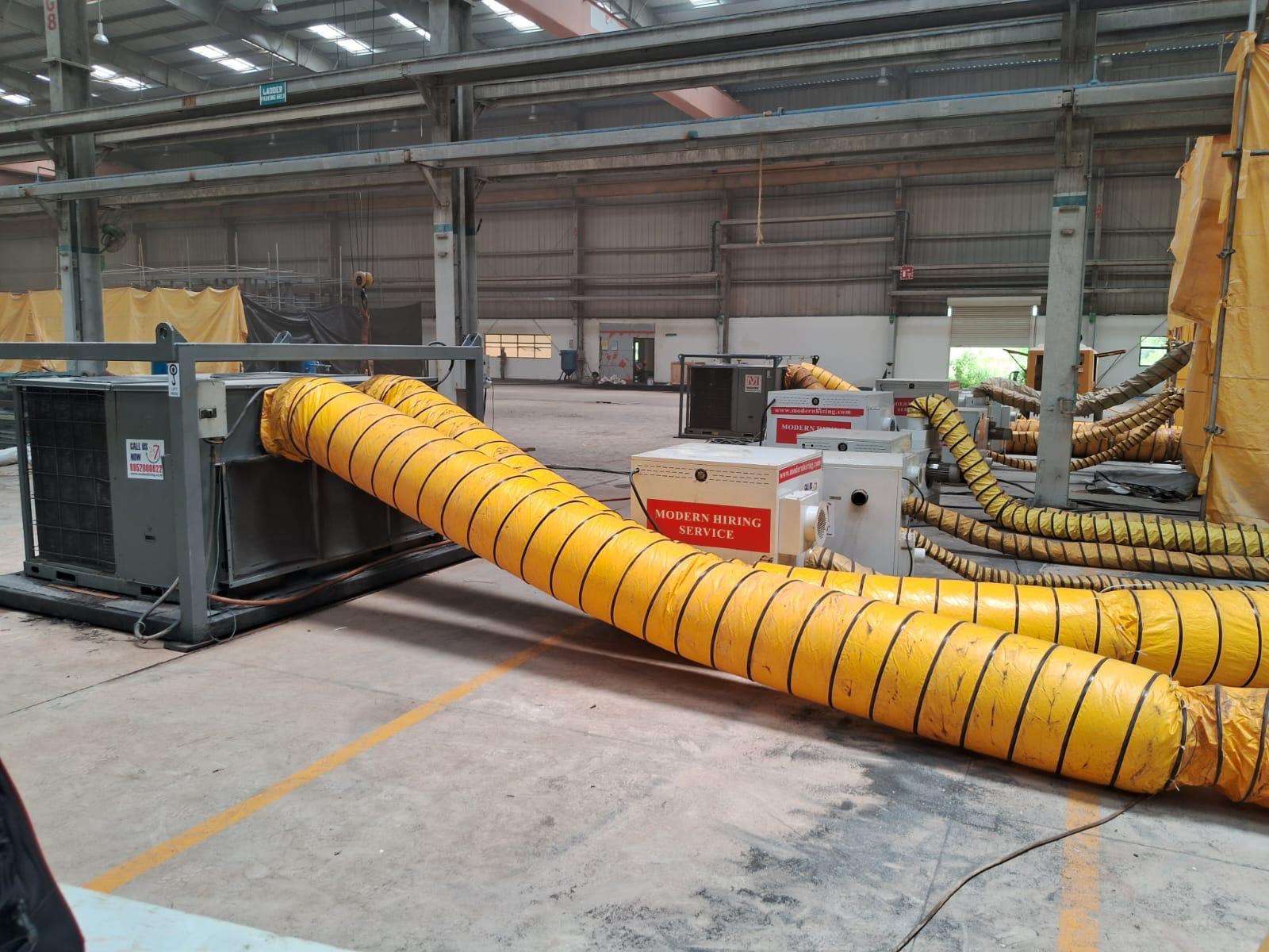 Industrial air conditioning units connected by large yellow flexible ducts inside a spacious warehouse.