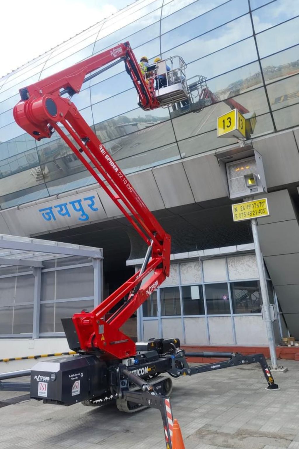 Two workers in high-visibility jackets elevated on a red hydraulic lift inspecting the tail section of a yellow and red airplane on a tarmac.