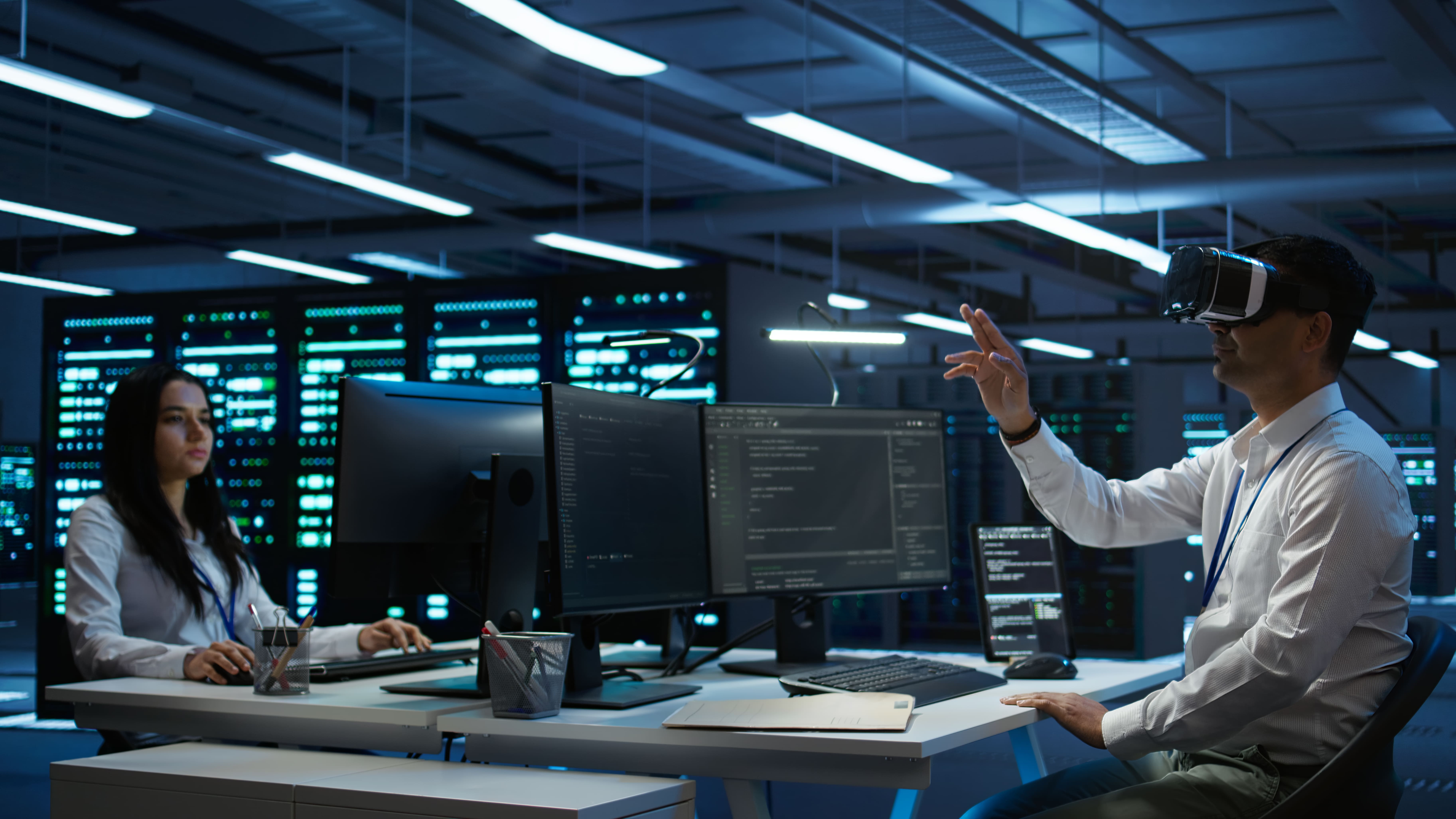 Industrial refinery complex with multiple tall metal towers and pipes illuminated at dusk against a clear blue sky.