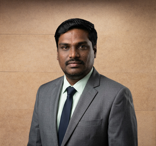 Man in gray suit, white shirt, and dark tie posing against a plain brown background.