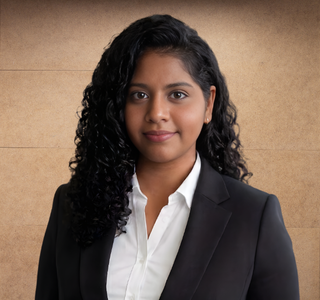 Portrait of a woman with curly black hair wearing a black blazer and white shirt against a beige background.