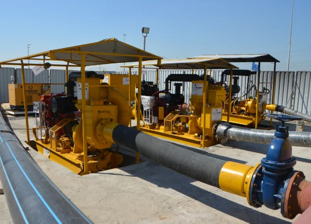 Three yellow industrial water pumps connected by large black hoses on a concrete surface under a clear blue sky.