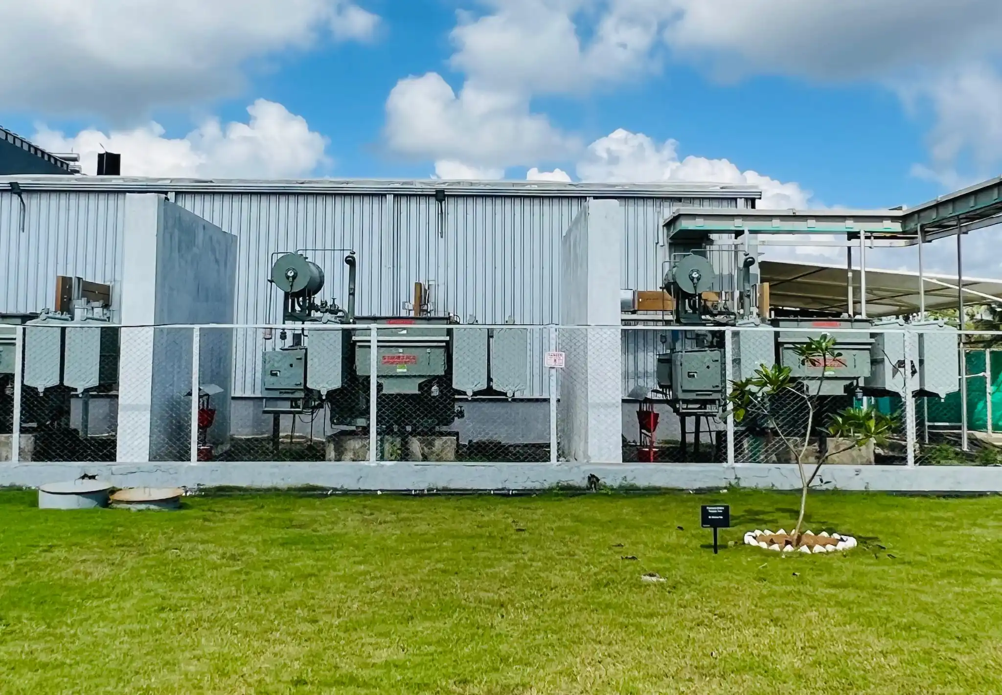 Three industrial machines installed outdoors against a building with a grassy lawn and partly cloudy sky above.