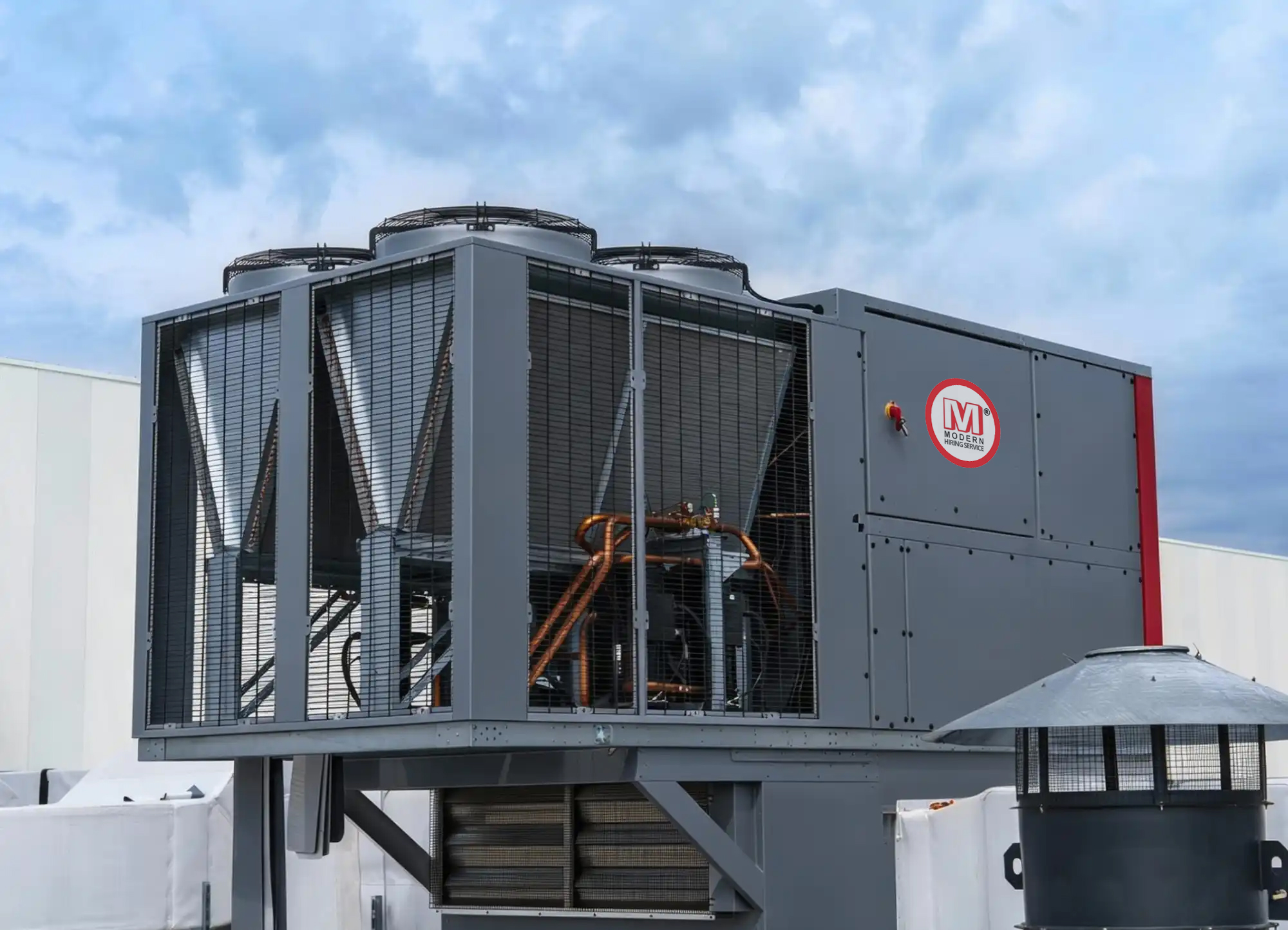 Large industrial HVAC unit with fans and copper piping installed outside a building under a partly cloudy sky.