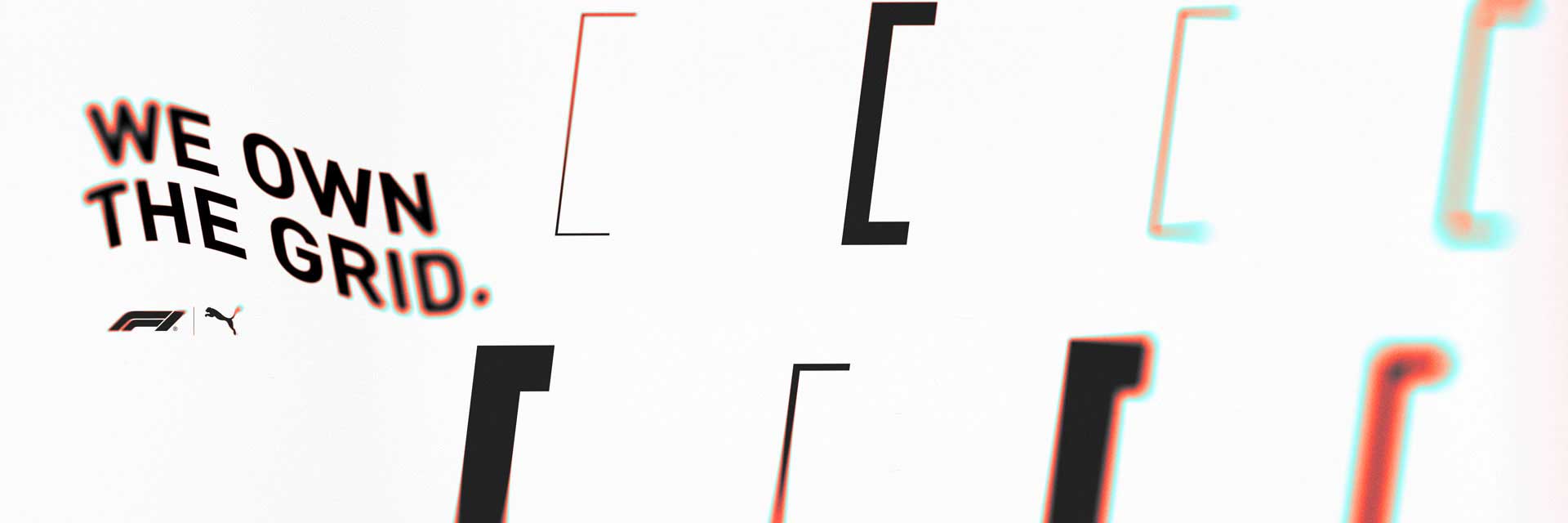 White wall with bold black text saying 'WE OWN THE GRID.' along with F1 and Puma logos.
