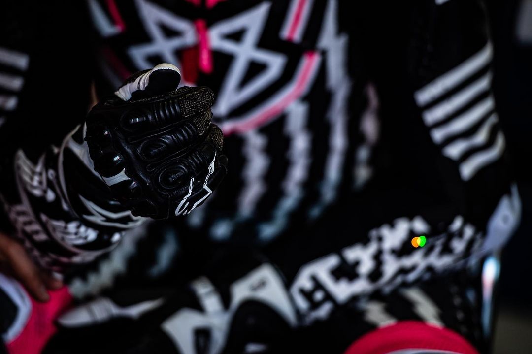Close-up of a person wearing black and white motorcycle gloves and a black outfit with white and pink patterns.