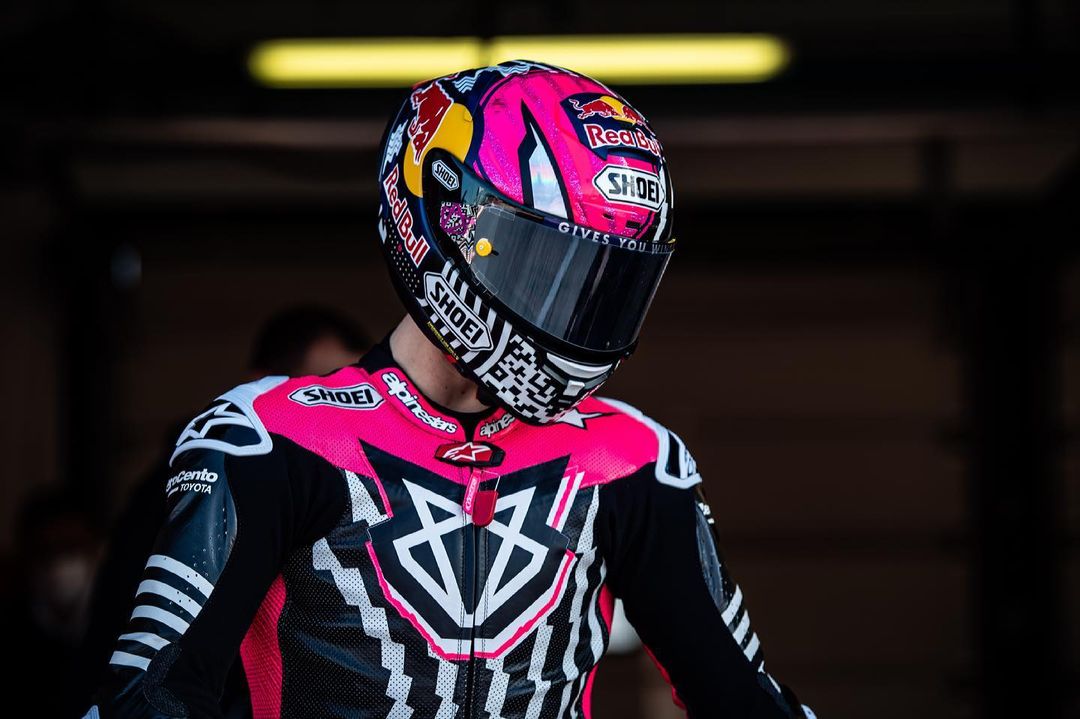 Race car driver in a black, pink, and white racing suit and helmet with Red Bull and Shoei logos.