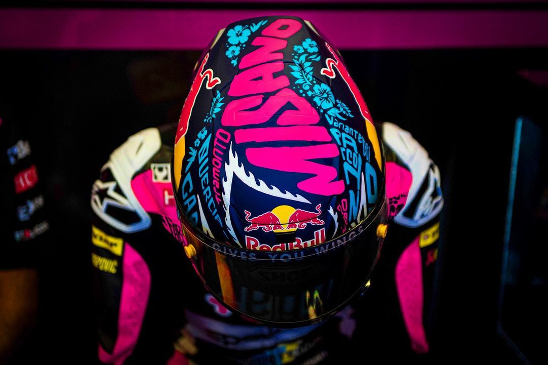 Racing helmet with vibrant pink and blue floral design and the word 'Misano', worn by a racer in a pink and white suit.