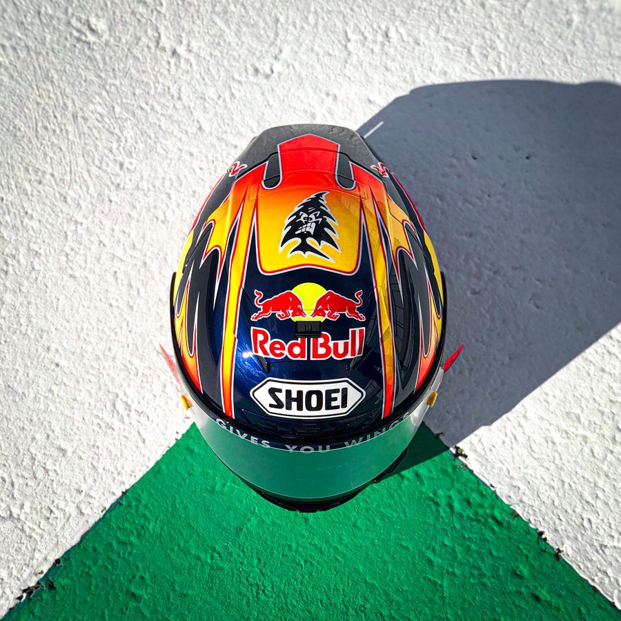 Top view of a colorful racing helmet with Red Bull and Shoei logos, placed on a textured surface with white and green-painted sections.