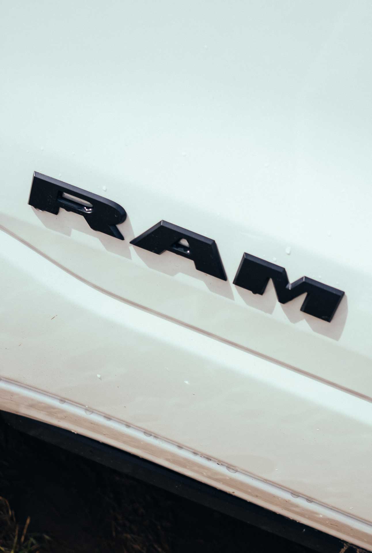 Close-up of black RAM emblem on a white vehicle surface with water droplets.