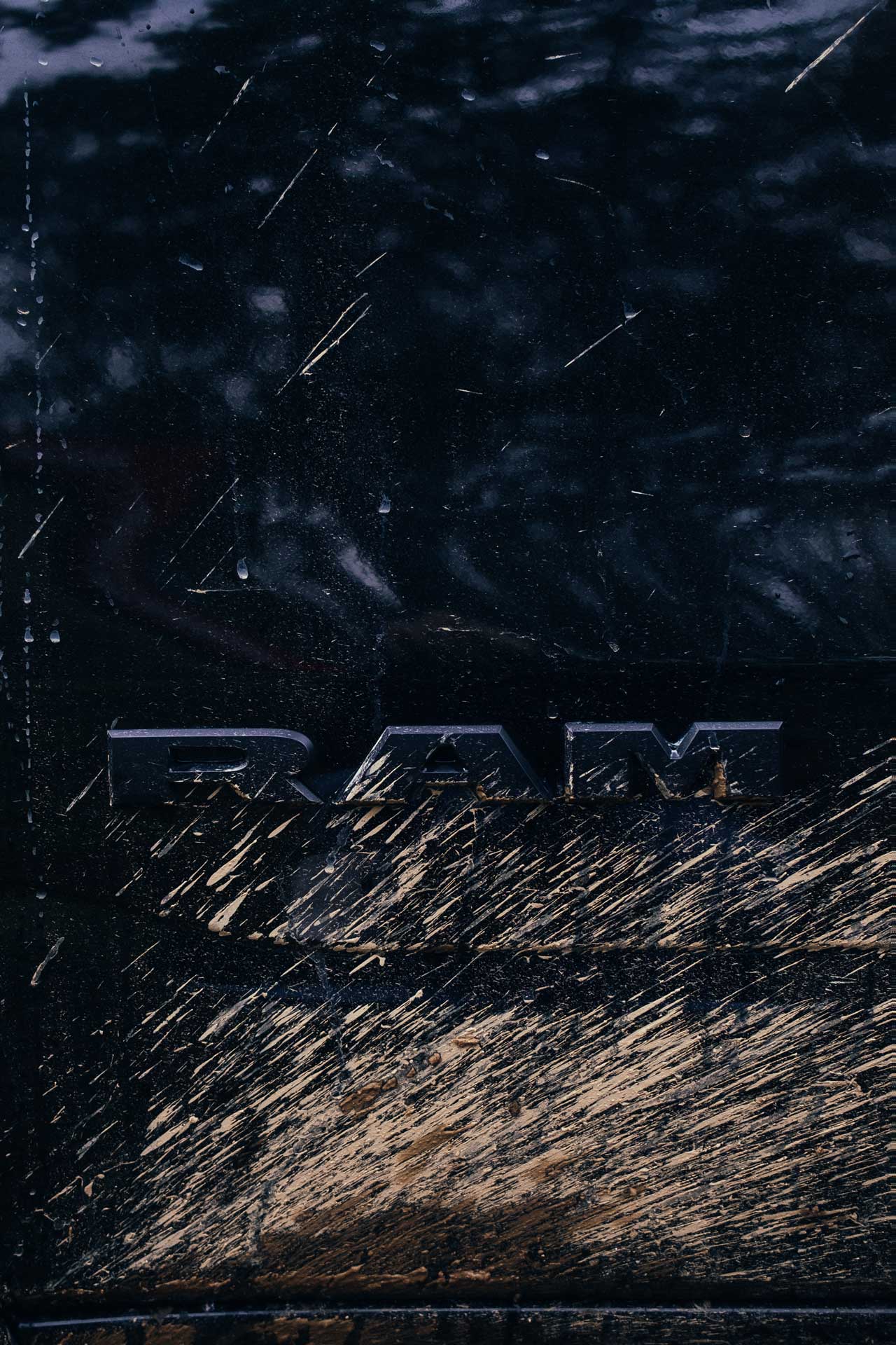 Close-up of a dirty black vehicle with mud splattered and 'RAM' emblem partially visible.
