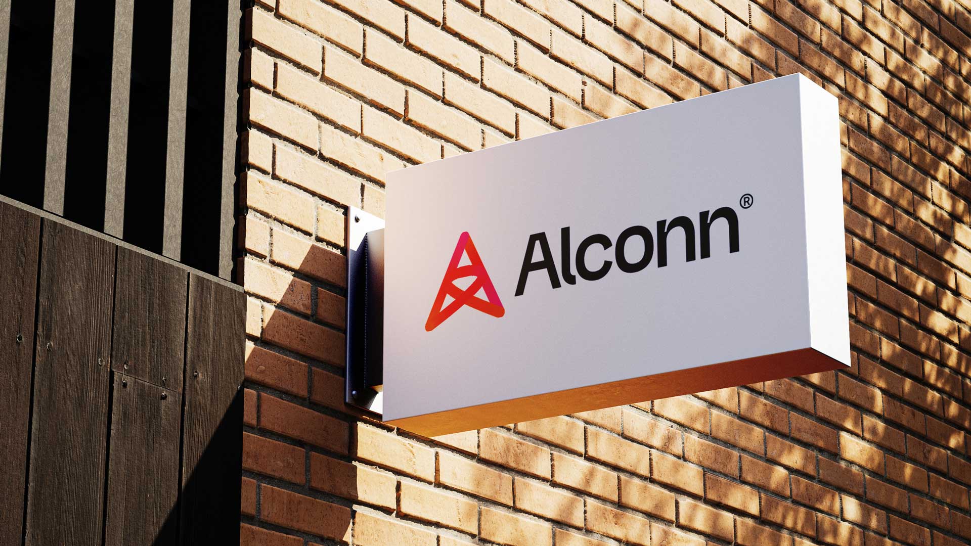 White rectangular sign mounted on a brick wall with a red and pink stylized A logo and the text 'Alconn'.
