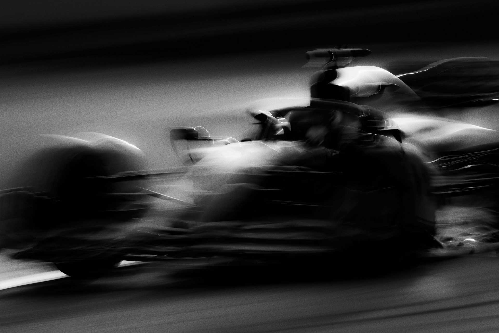 Black and white motion-blurred image of a Formula 1 race car speeding on a track.
