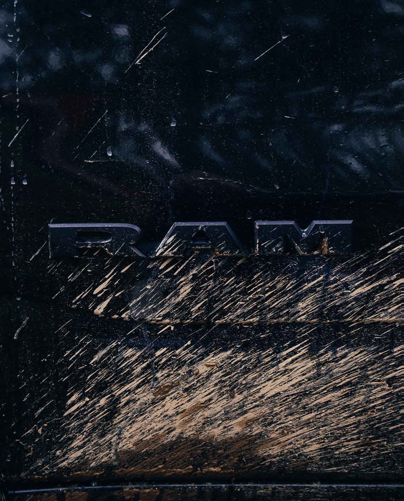Close-up of a black vehicle with the RAM logo partially covered in mud and dirt splatters.