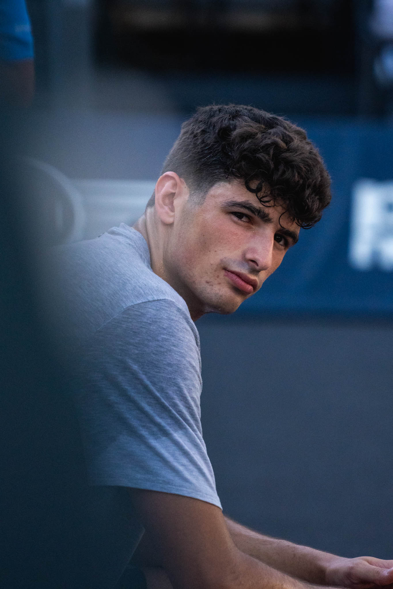 Young man with curly hair and a gray t-shirt looking over his shoulder.
