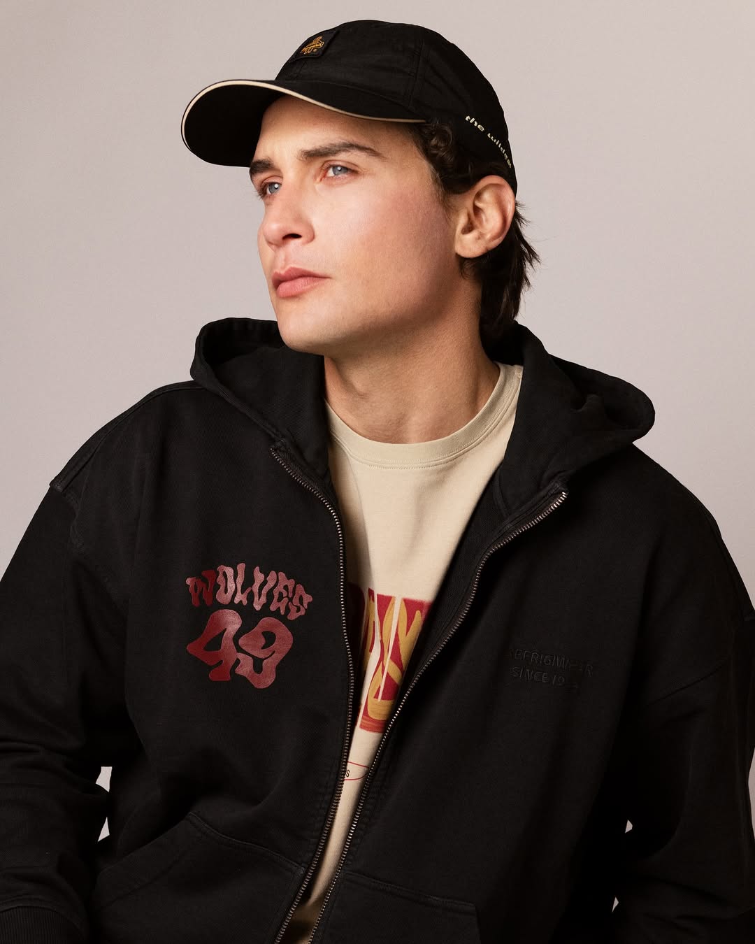 Young man wearing a black cap and black zip-up hoodie with 'Wolves 49' text in red, looking to the side.