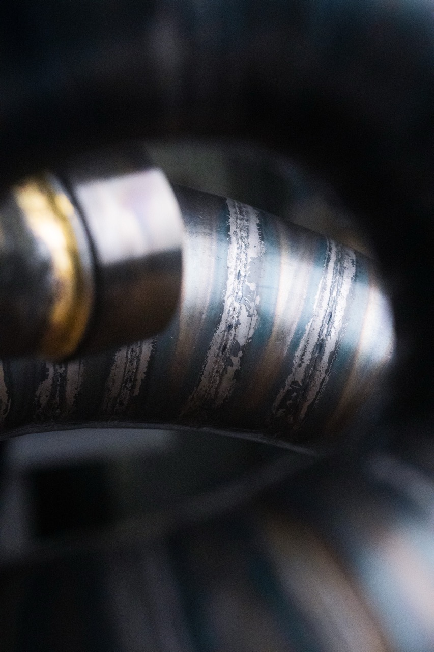 Close-up of a metal pipe with visible welding marks and a blurred metal fitting.