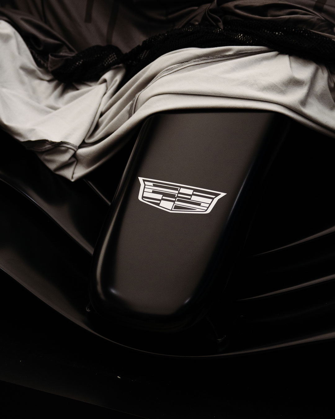 Close-up of a black car hood featuring the white Cadillac emblem partially covered by a gray cloth.