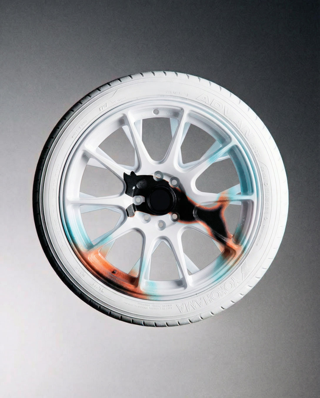 White alloy car wheel with black, turquoise, and orange paint design resembling a puma silhouette on the rim.