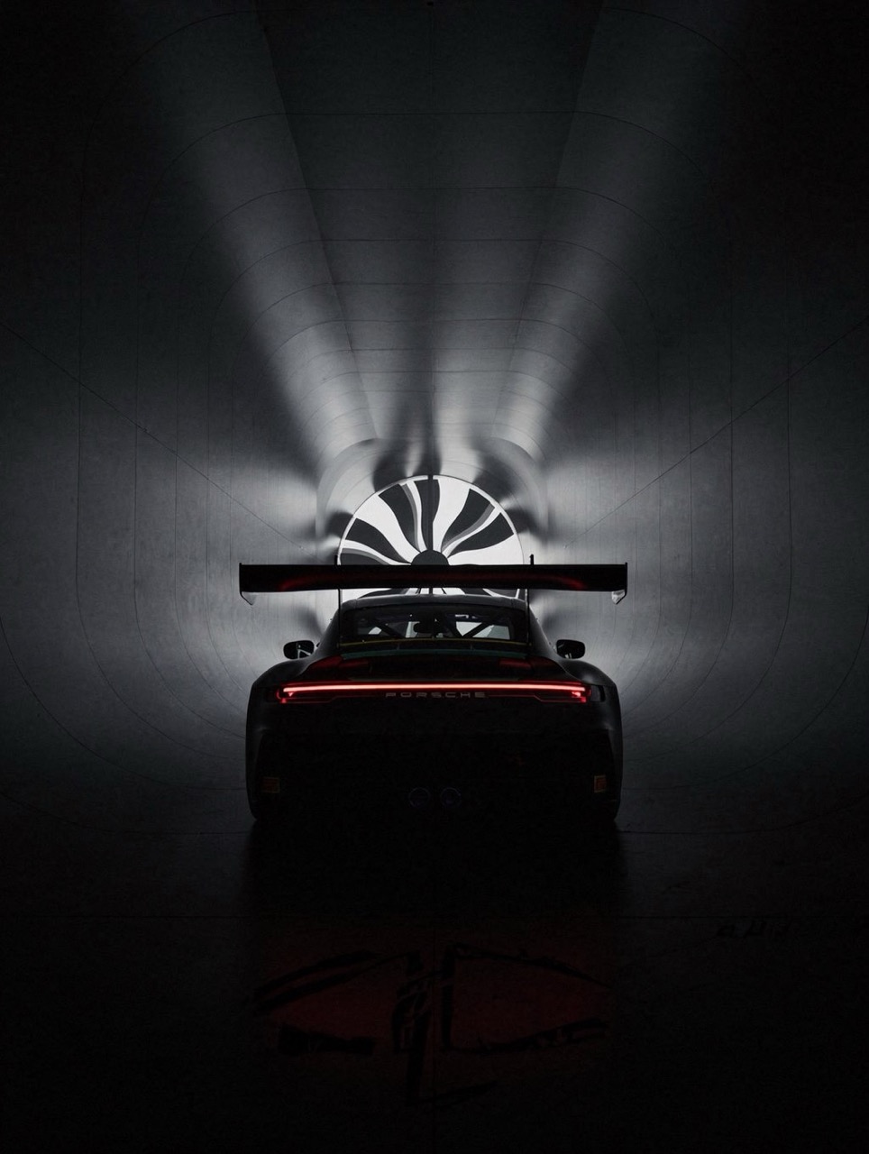 Rear view of a Porsche race car inside a wind tunnel with fan blades visible in the background.