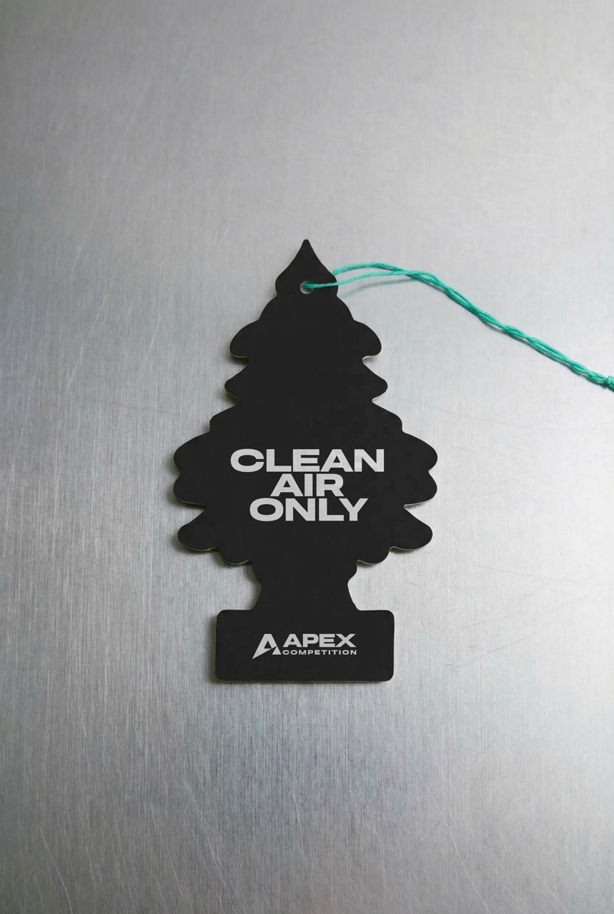 Black tree-shaped air freshener with words 'CLEAN AIR ONLY' and 'APEX COMPETITION' on a metallic surface.