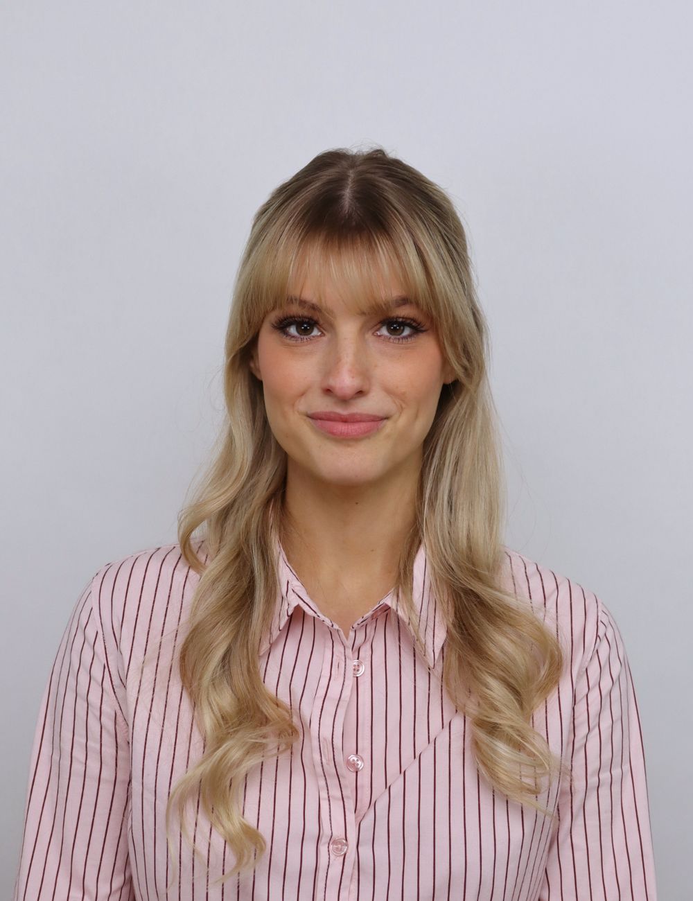Smiling young man in a gray suit and white shirt standing outdoors in front of a house.