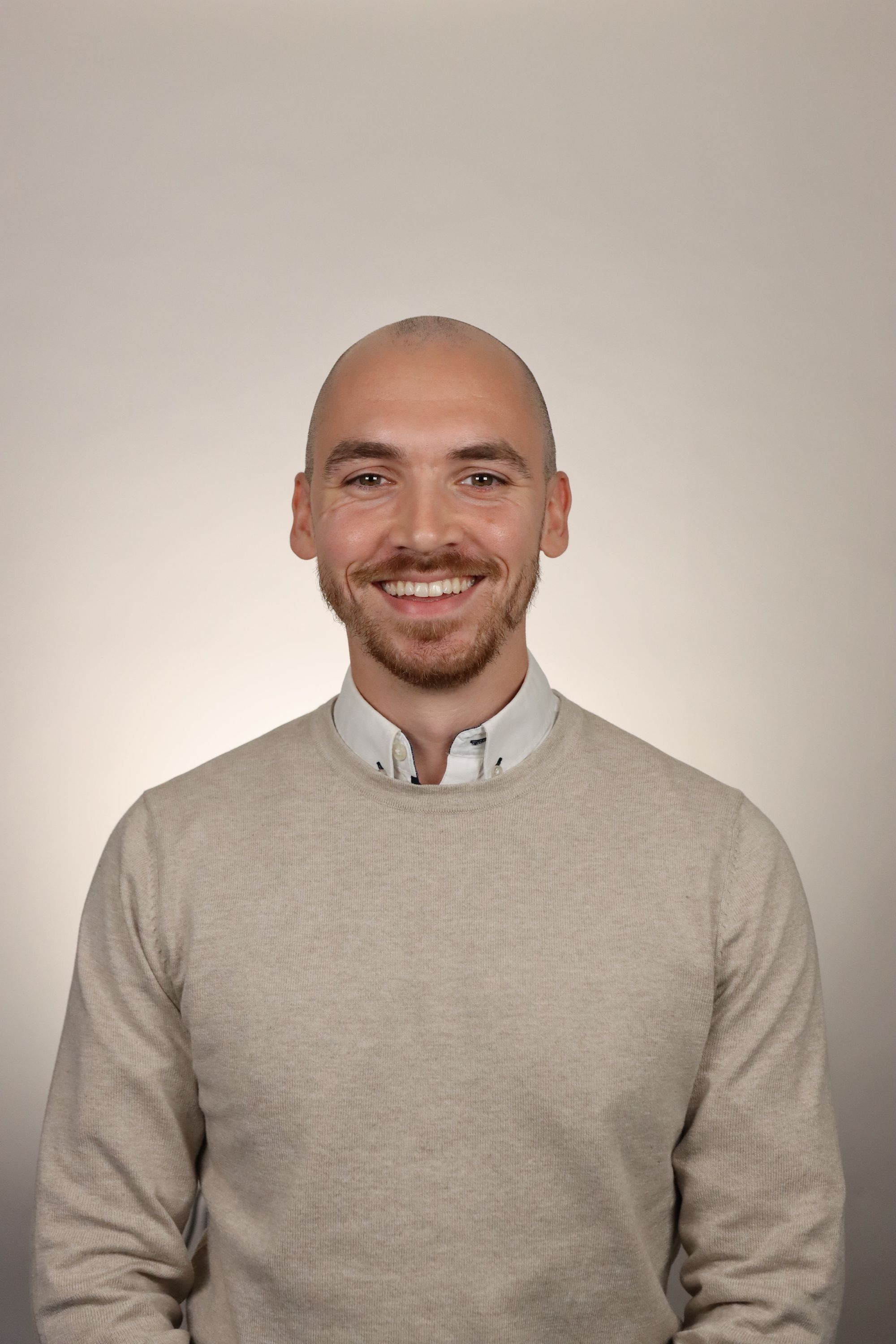 Smiling young man in a gray suit and white shirt standing outdoors in front of a house.