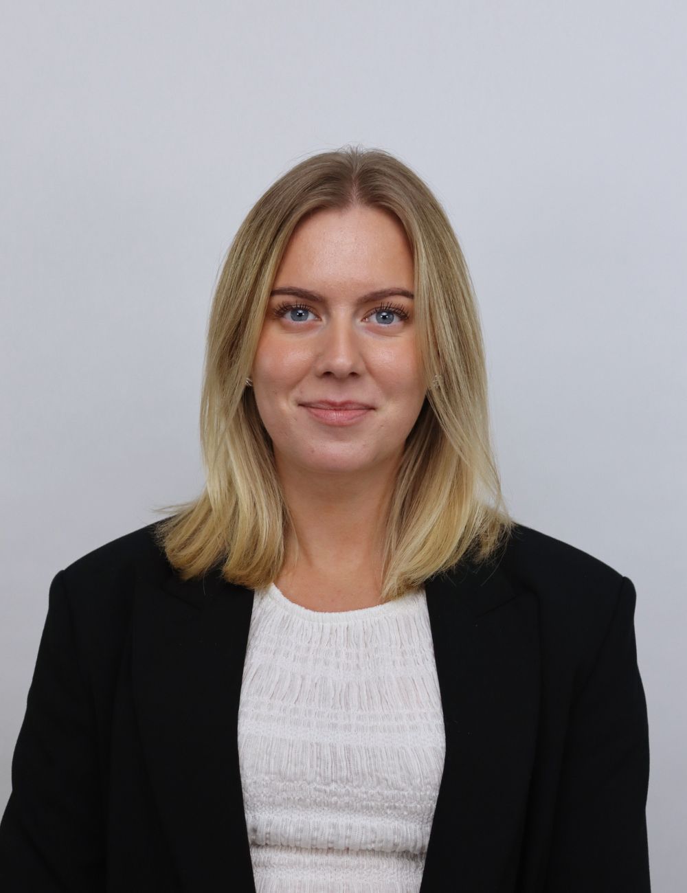 Smiling woman with long wavy blonde hair wearing a black blazer standing with crossed arms in front of a bookshelf.