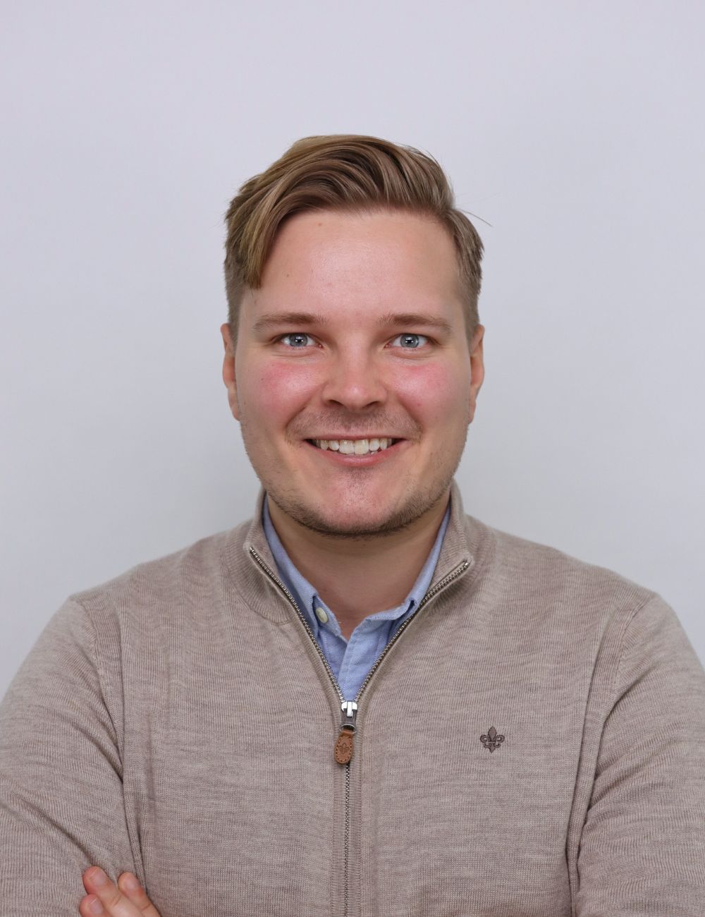 Smiling man with styled hair wearing a black jacket and light blue shirt standing in front of a city skyline.