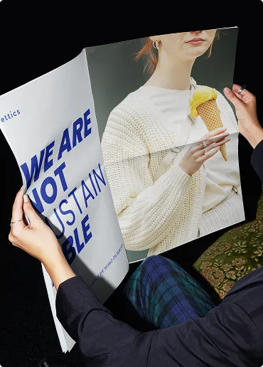 Person hält Magazin aufgeschlagen, auf einer Seite steht großer blauer Text 'WE ARE NOT SUSTAINABLE', auf der anderen Seite ist Bild einer Person mit gelbem Eis in Waffel.