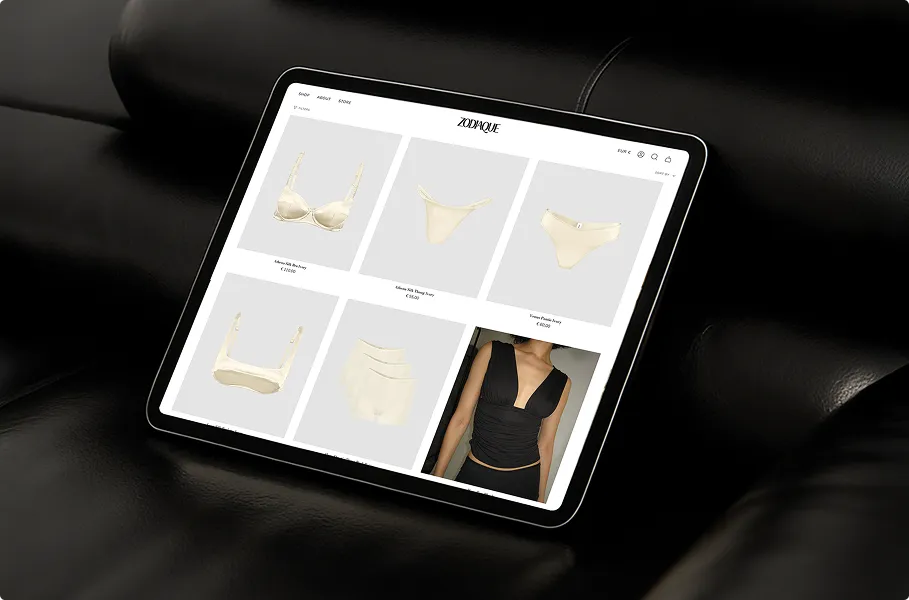 Tablet auf schwarzem Leder sitzt und zeigt eine Website mit beiger Damenunterwäsche und einem schwarzen Oberteil.