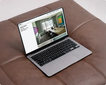 Offener Laptop mit einer Webseite, die ein modernes Besprechungszimmer zeigt, auf einem braunen Ledersofa.