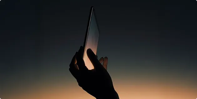 Silhouette einer Hand, die ein Smartphone gegen einen Himmel bei Sonnenuntergang hält.