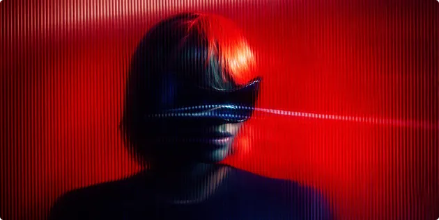 Person mit kurzem Haar trägt eine schwarze Virtual-Reality-Brille vor rotem Hintergrund mit verschwommenem Lichteffekt.
