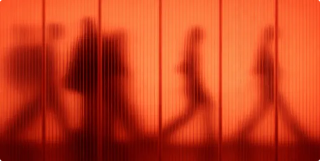 Verschwommene Schatten von Menschen, die hinter einer strukturierten roten Wand gehen.