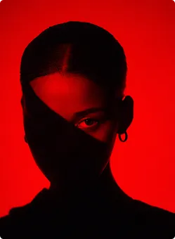 Porträt einer Frau mit dunklem Schatten, der ihr Gesicht teilt, vor rotem Hintergrund.