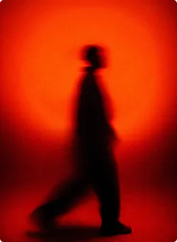 Verschwommene Silhouette einer gehenden Person vor rotem Hintergrund.