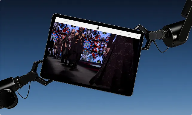 Tablet wird von zwei mechanischen Armen gehalten, zeigt eine Modenschau mit Models auf dem Laufsteg vor einem farbenfrohen Hintergrund.