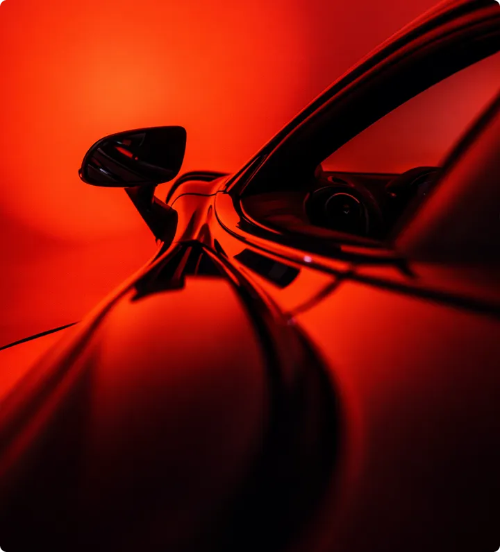 Nahaufnahme eines schwarzen Autos mit roten Lichtreflexionen, Schwerpunkt auf der Seite und dem Seitenspiegel.